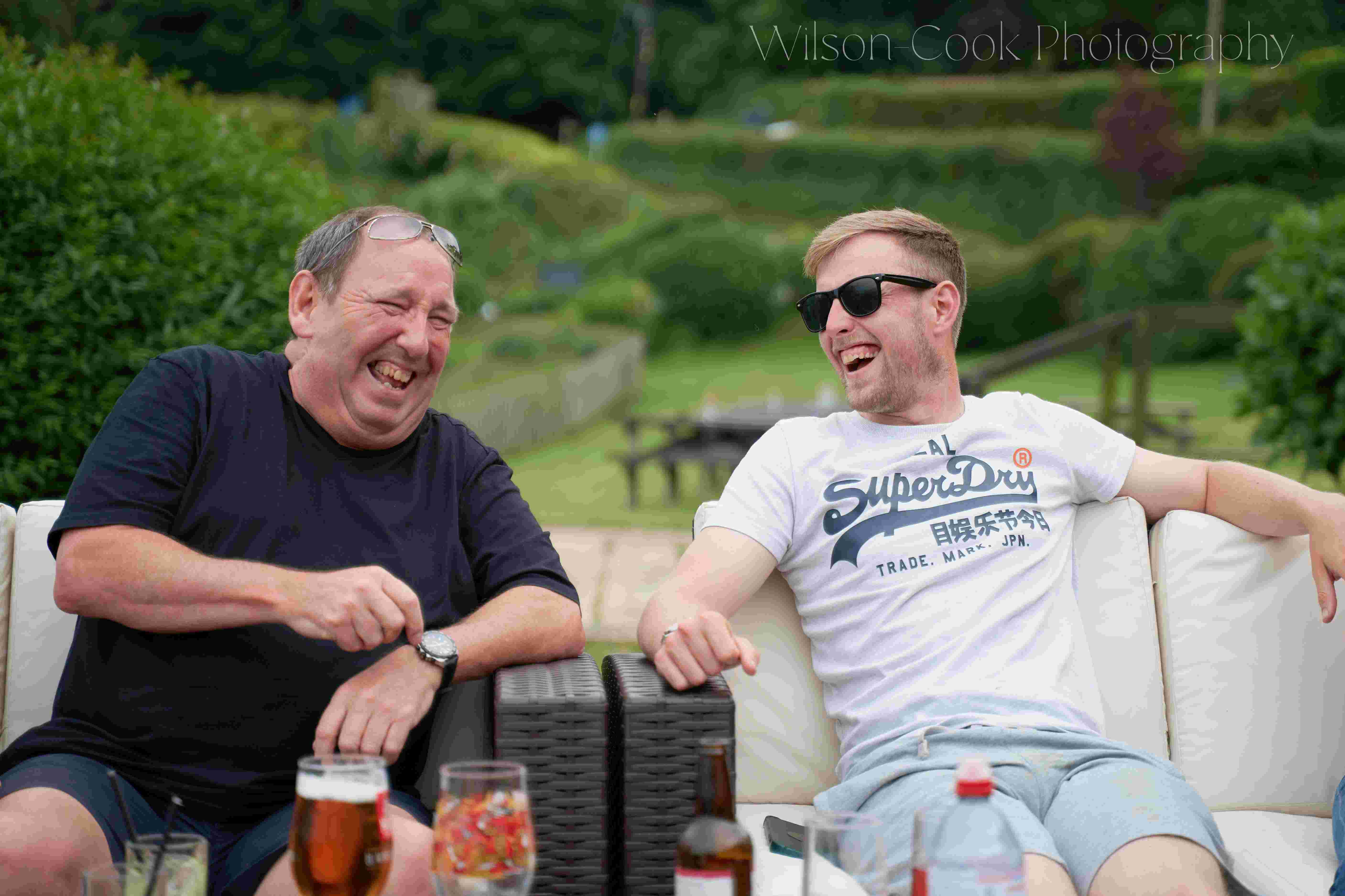 Two people laughing, in front of a garden.
