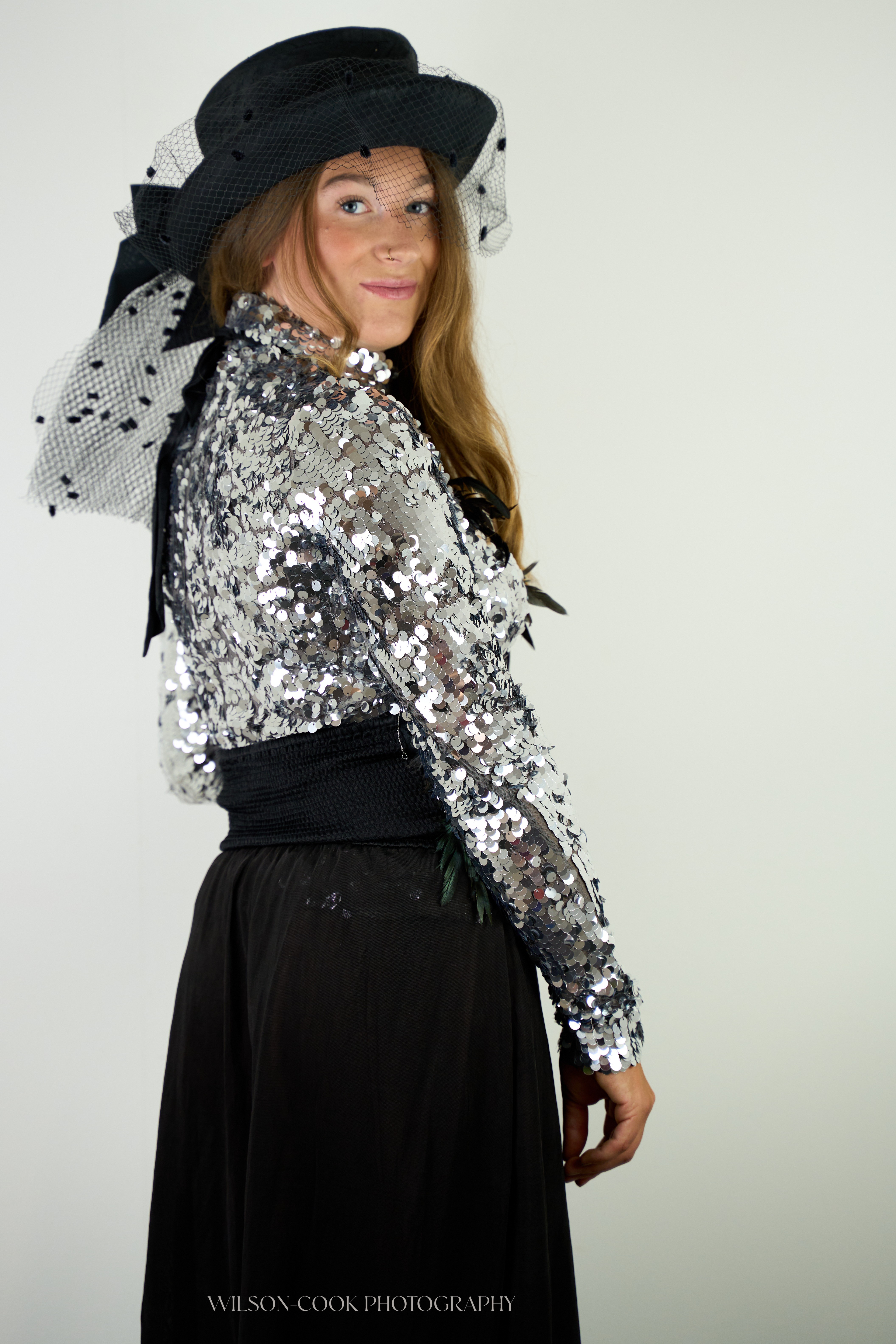 2025.  A woman in a silver sequin outfit looks over her right shoulder at the camera