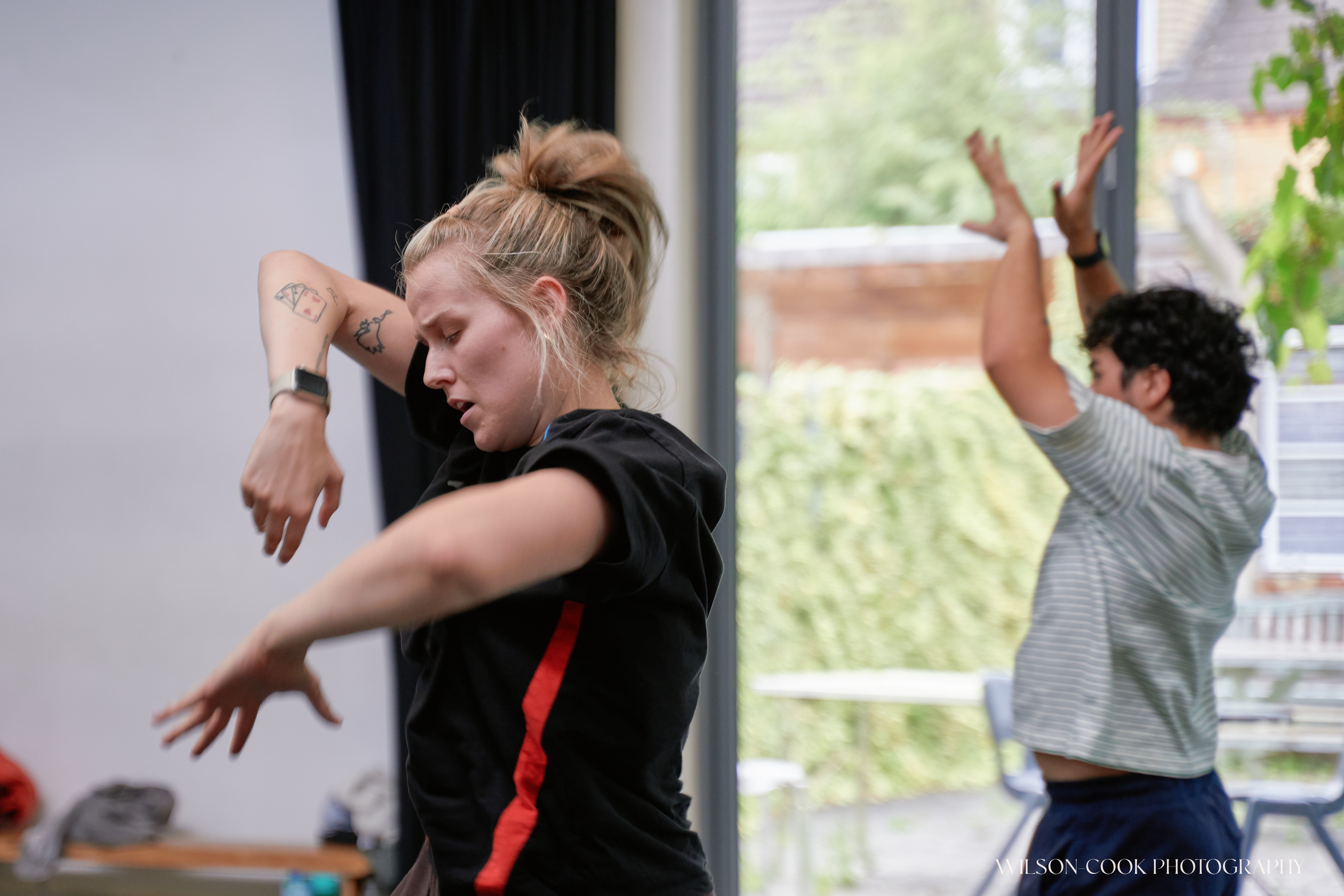 2025.  Two dancers are captured mid-movement, both are facing towards the left of the image, with their arms in interesting positions.