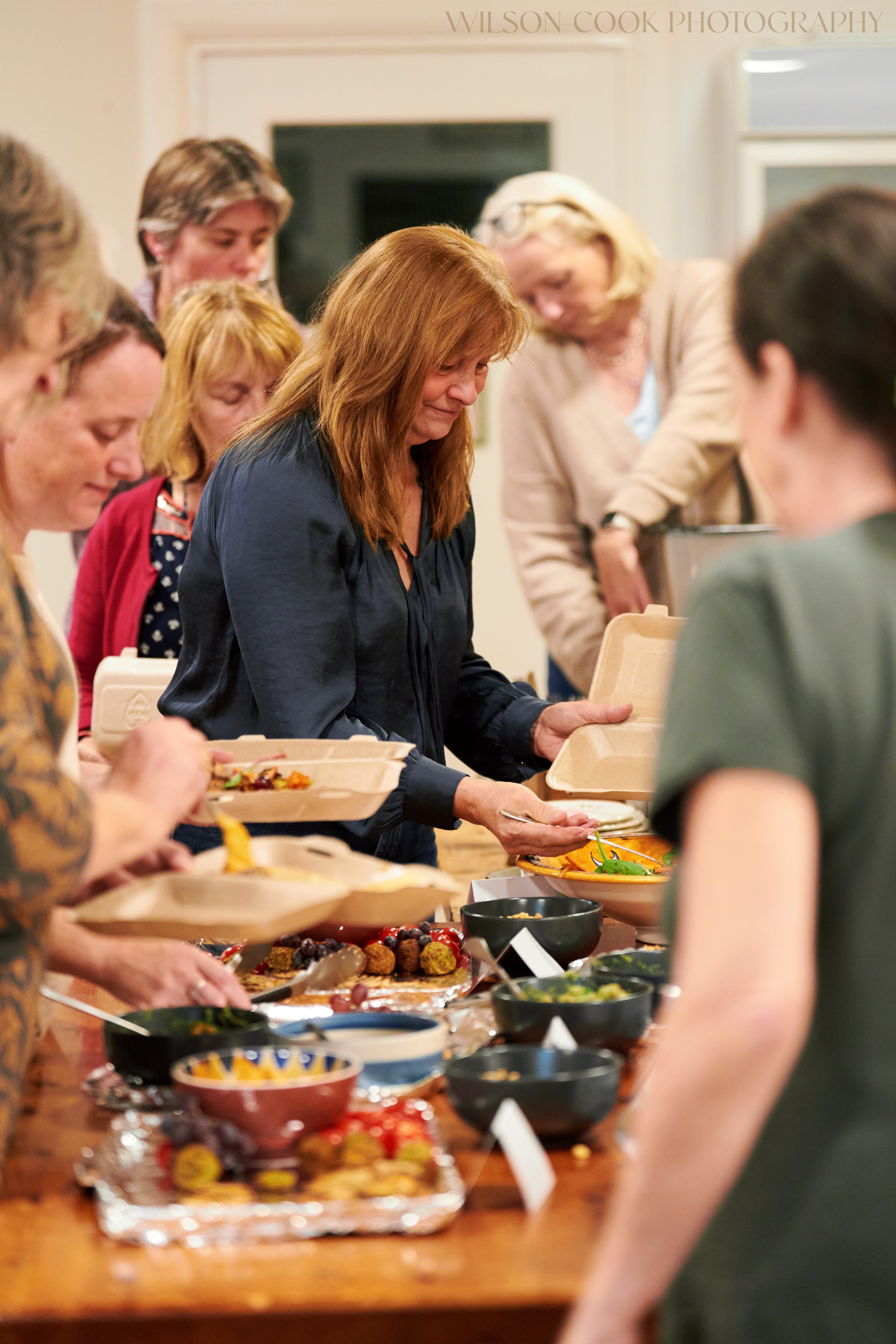 2025.  A group of women queue at a table at a community event