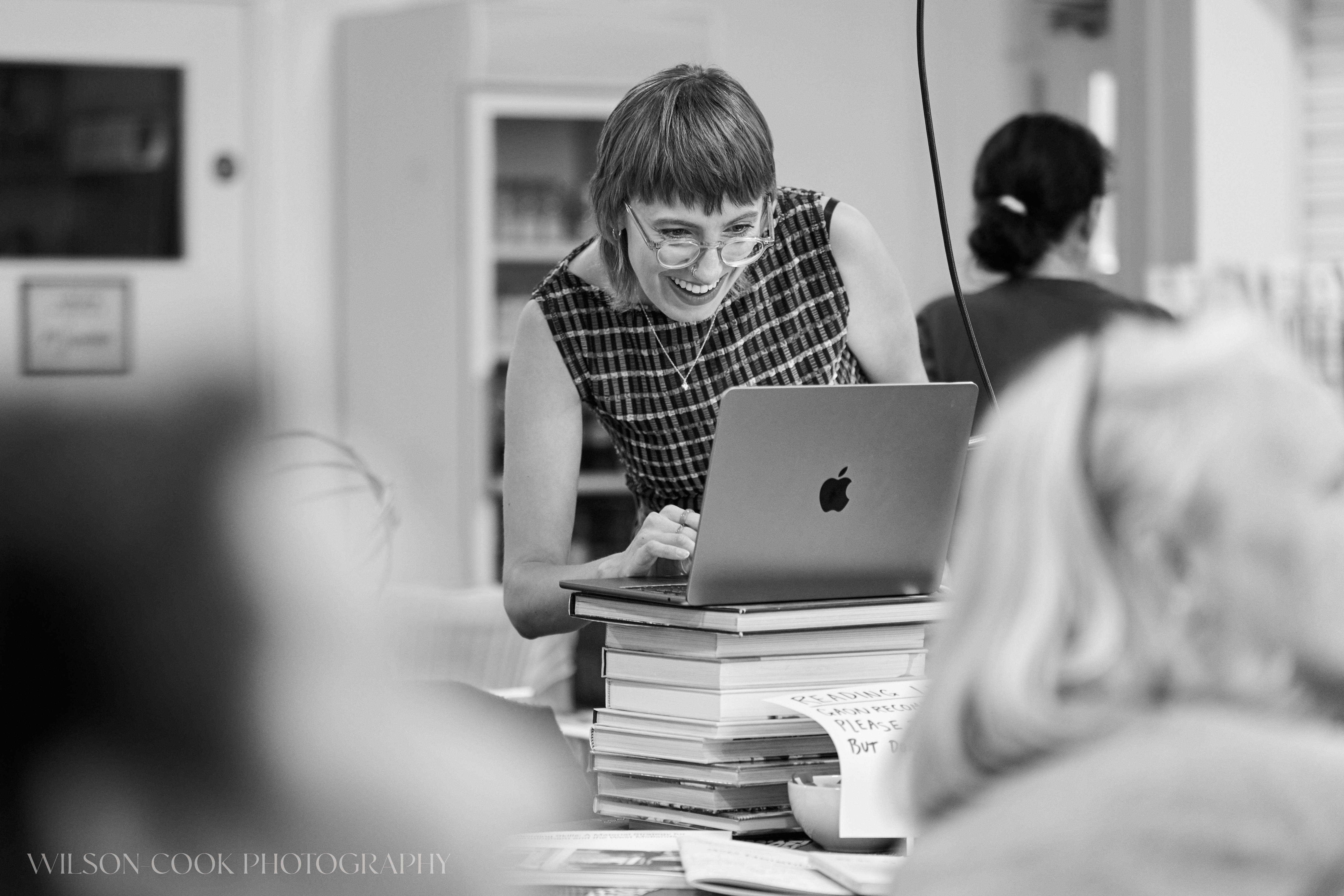 2025.  The facilitator of a community event smiles while using her laptop, in black and white